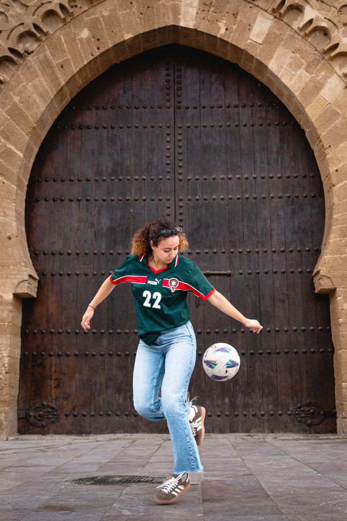 A woman skillfully controls a soccer ball in front of a historic arched door.