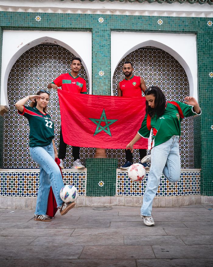 Group of Moroccan soccer fans posing with flag and footballs near traditional architecture outdoors.